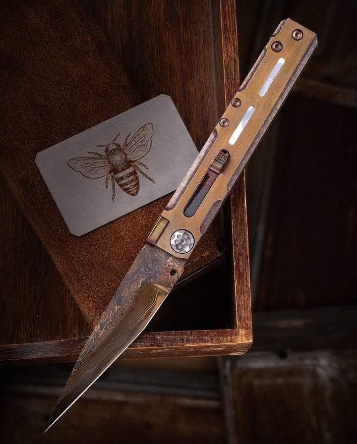 Bronze-toned handle and flowing patterned steel beside an engraved bee card
